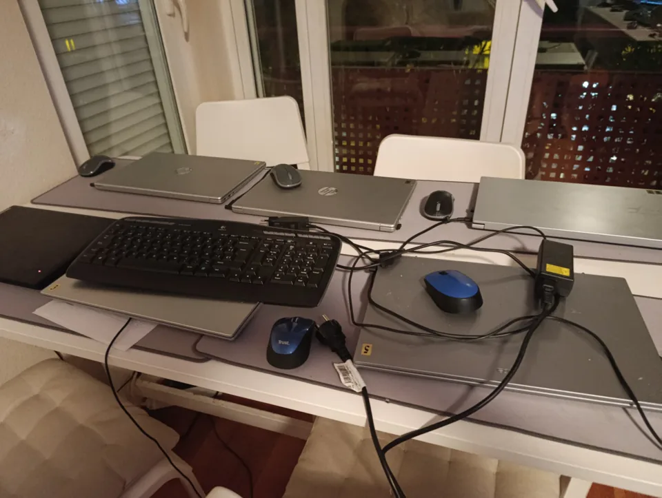 Varios portátiles con teclado y ratón sobre una mesa larga, junto a la ventana